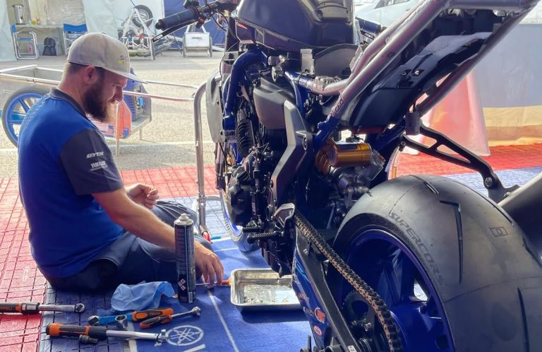 A mechanic works on the rear of a motorcycle, surrounded by tools and equipment.